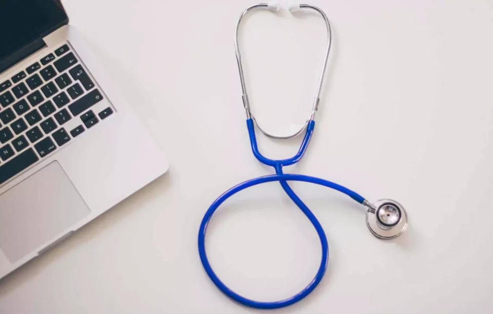 Blue stethoscope and the laptop on the white surface