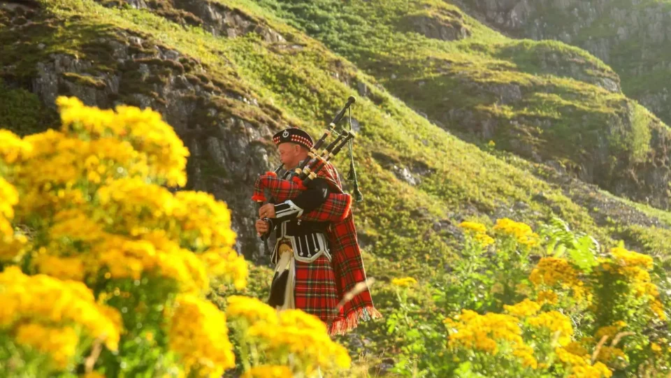 Man on a field plays the bagpipes 