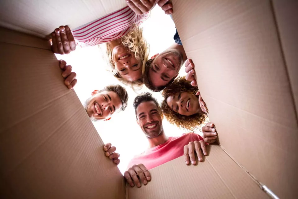 Five people looking at the camera through a cardboard box after international moving