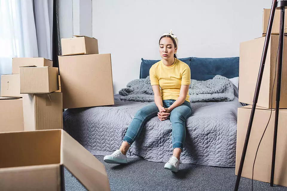 Sad woman sitting on a bed surrounded by boxes