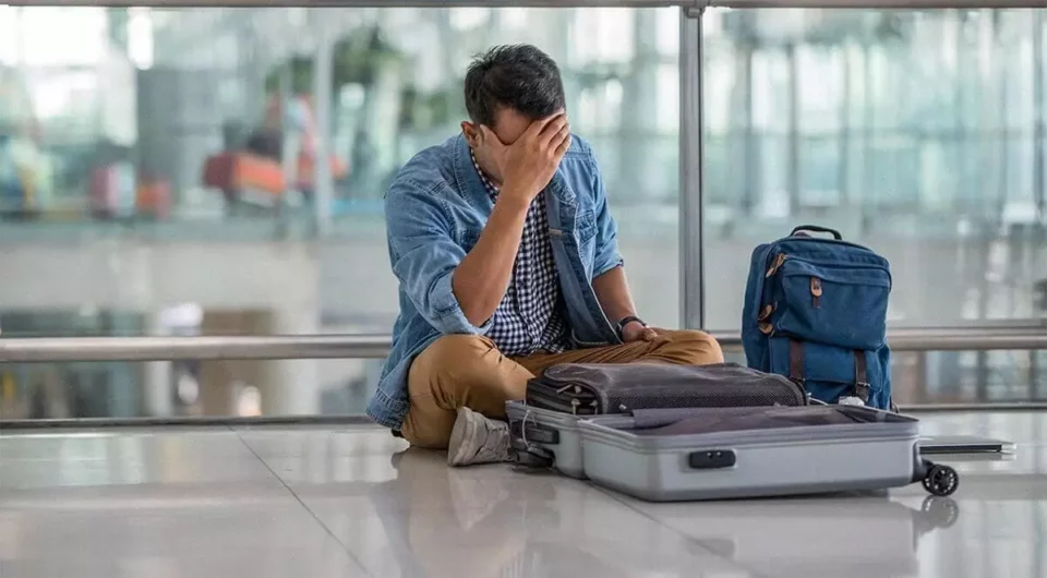 A man looking at his suitcase and holding his head