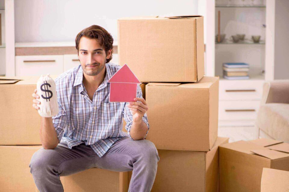a man sitting next to boxes holding a house