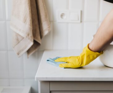 A woman in yellow gloves wiping the sink