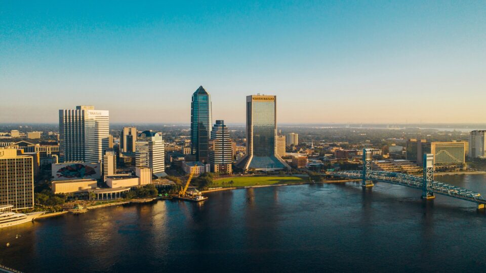 Aerial drone view of the Jacksonville city skyline under a clear blue sky in Florida.