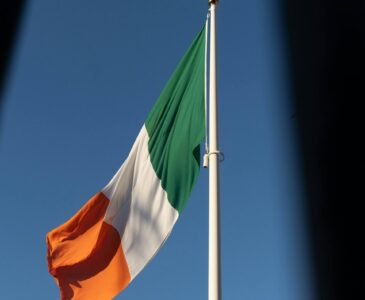 The national flag of Ireland with vertical green, white, and orange stripes waving in the wind.
