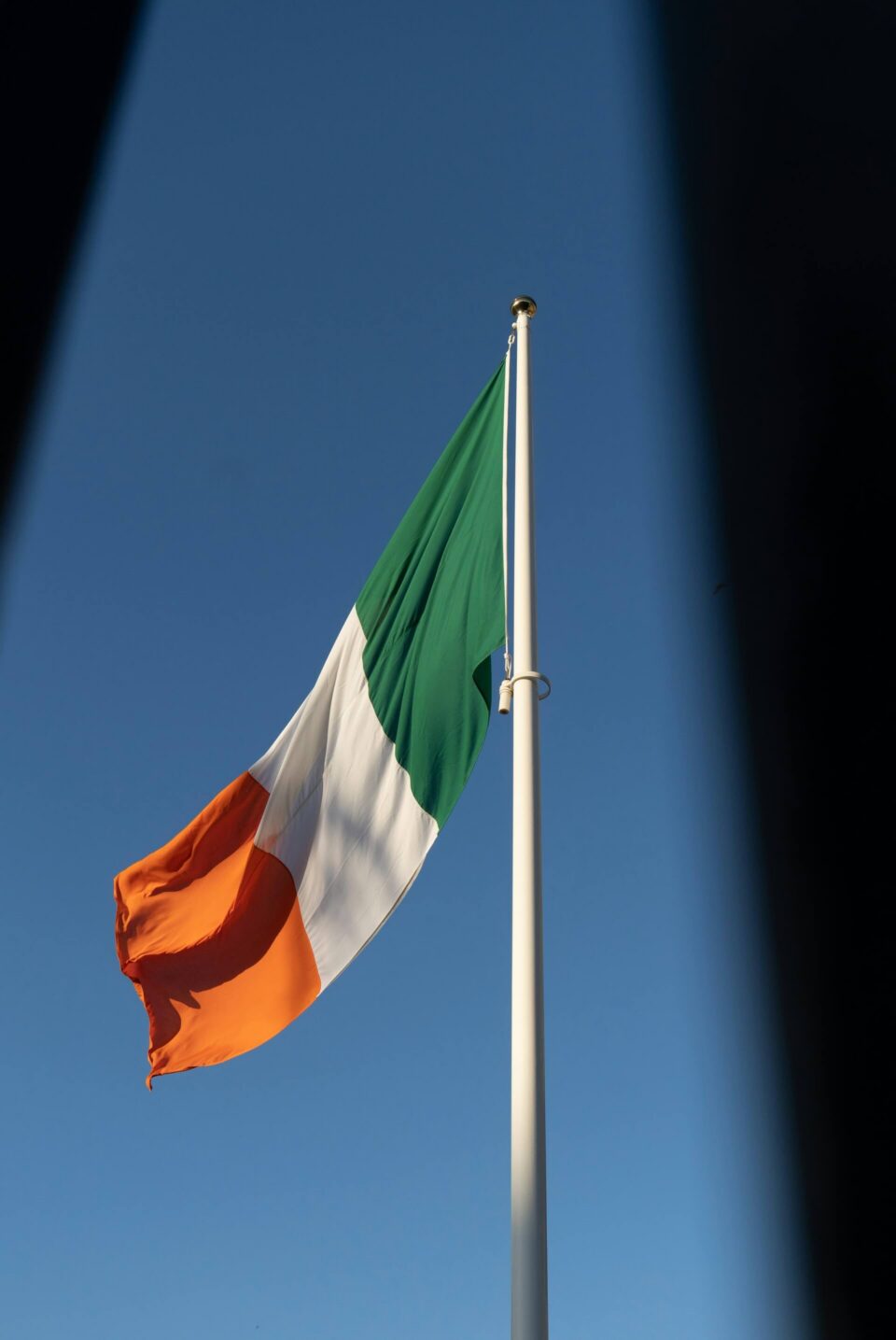The national flag of Ireland with vertical green, white, and orange stripes waving in the wind.